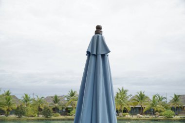 Mavi şemsiye bir evin önünde duruyor. Şemsiye açık ve gökyüzü bulutlu.