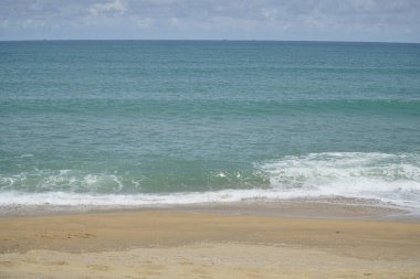 Okyanus sakin ve gökyüzü bulutlu. Su koyu mavi bir renktir. Kumsal kumlu ve dalgalar küçük