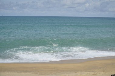 Okyanus sakin ve gökyüzü bulutlu. Su koyu mavi bir renktir. Kumsal kumlu ve dalgalar küçük