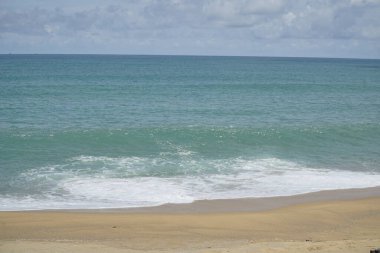 Okyanus sakin ve gökyüzü bulutlu. Su mavinin güzel bir tonu. Kumsal boş ve dalgalar küçük.