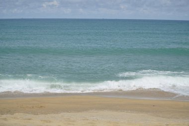 Okyanus sakin ve gökyüzü bulutlu. Kumsal boş ve su da mavinin güzel bir tonu.