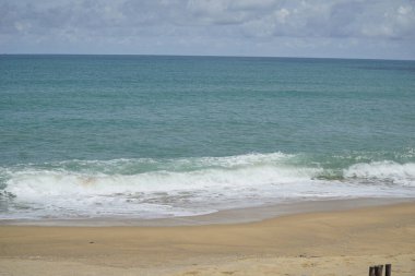 Okyanus sakin ve gökyüzü bulutlu. Kumsal boş ve dalgalar küçük.