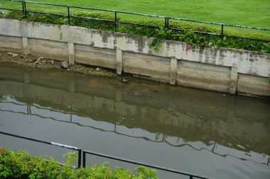 Kenarları çitle çevrili kirli bir nehir. Su bulanık ve çit siyah.