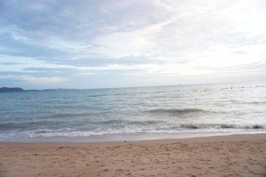 Sahil sakin bir okyanus ve bulutlu bir gökyüzü. Gökyüzü mavi ve gri karışımı. Sahneye huzurlu ve huzurlu bir atmosfer veriyor.