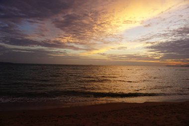 Güneş okyanusun üzerinde batarken gökyüzü güzel turuncu bir renktir. Su sakin ve kumsal boş.