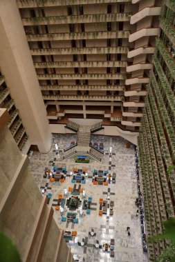 Yeşil duvarı ve merdivenleri olan büyük bir otel lobisi. Lobi insan ve sandalyelerle dolu.