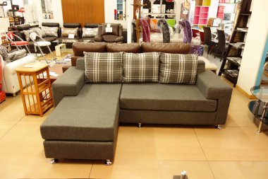 Ekose yastıklı gri bölmeli kanepe bir galeride duruyor. Kanepe ahşap bir masa ve birkaç sandalye de dahil olmak üzere diğer mobilyalarla çevrilidir. Odanın modern ve şık bir havası var.