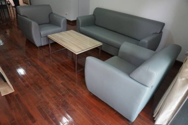 Gri bir kanepesi, iki sandalyesi ve ahşap bir sehpası olan oturma odası. Odanın samimi ve davetkar bir atmosferi var.