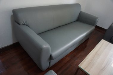 Gri kanepe bir odada, ahşap bir zeminde oturur. Kanepe deriden yapılmıştır ve görüntünün odak noktasıdır.