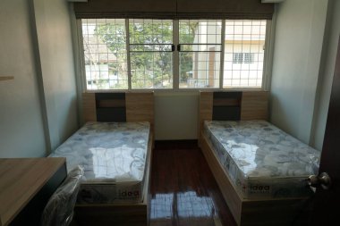 İki yataklı ve masalı bir yatak odası. Yataklar hazır ve oda temiz. Pencereler doğal ışık veriyor ve oda basit, minimalist bir hisse sahip.