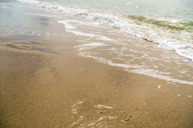 Sahil sakin ve sakin. Arka planda hafif bir dalga var. Kum kuru ve su berrak.