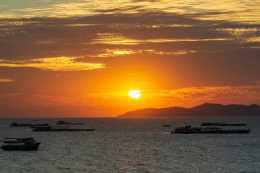 Güneş okyanusun üzerinde batıyor, suyun üzerine sıcak bir parıltı saçıyor. Gökyüzü bulutlarla dolu, sakin ve huzurlu bir atmosfer yaratıyor. Sudaki tekneler dağıtıldı.