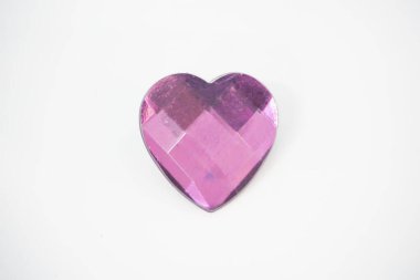 Kalp şeklinde mor kristal broş beyaz bir zeminde durur. Broş camdan yapılmıştır ve parlak, yansıtıcı bir yüzeye sahiptir. Broşun rengi morun derin bir tonu.