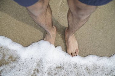 Adamın ayakları suyun içinde, kıyıda köpük var. Rahatlama ve rahatlama kavramı, adam plajın ve suyun tadını çıkarırken.