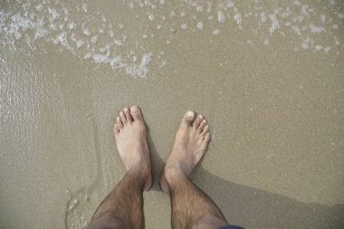 Adamın ayakları sahilde, arka planda su var. Rahatlama ve rahatlama kavramı, adam yalın ayak ve plajın tadını çıkarıyor.
