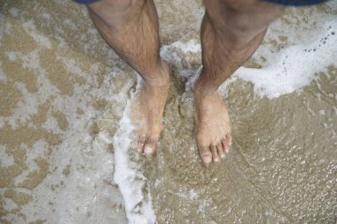 Adamın ayakları suyun içinde, dalgalar onu sarsıyor. Rahatlama ve sükunet kavramı, adam okyanusta yalınayak dururken