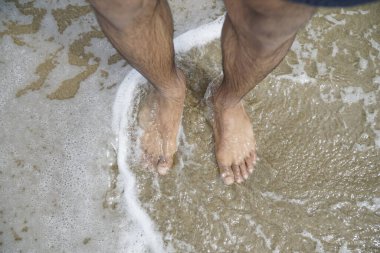 Adamın ayakları suyun içinde, ayak parmakları dışarıda. Su dalgalı ve adamın bacakları görünür durumda.