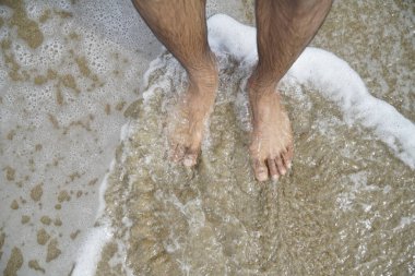 İnsanın ayakları suyun içinde, etrafındaki dalgalar çarpıyor. Rahatlama ve rahatlama kavramı, adam plajın ve suyun tadını çıkarırken.