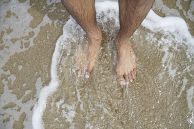 İnsanın ayakları suyun içinde, ve su köpüklü. Rahatlama ve rahatlama kavramı, adam plajın ve suyun tadını çıkarırken.