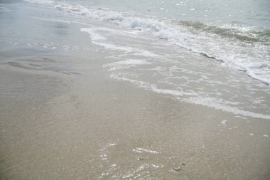 Kumsal sakin ve huzurlu, dalgalar yavaşça kıyıya vuruyor. Kum açık ten rengidir ve su açık mavi renktedir. Sahne huzurlu ve rahatlatıcı.