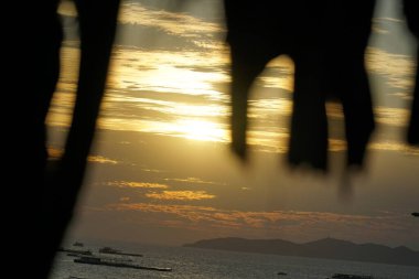 Güneş okyanusun üzerinde batıyor, suyun üzerine sıcak bir parıltı saçıyor. Gökyüzü bulutlarla dolu. Huzurlu ve huzurlu bir atmosfer yaratıyor.