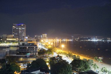 Geceleri arka planda plaj olan bir şehir. Şehir ışıklarla aydınlandı ve sahil de aydınlandı.