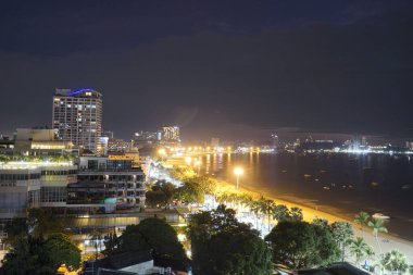 Geceleri arka planda plaj olan bir şehir. Şehir ışıklarla aydınlandı ve sahil de aydınlandı.