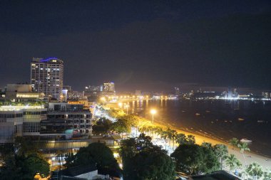 Geceleri arka planda plaj olan bir şehir. Şehir ışıklarla aydınlandı ve sahil de aydınlandı.