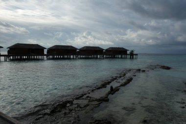 Sahilde küçük tahta kulübeleri olan bir sahil. Su sakin ve gökyüzü bulutlu.