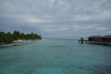 Uzakta küçük bir ahşap iskelesi olan güzel mavi bir okyanus. Gökyüzü bulutlu, ama su sakin ve davetkar.