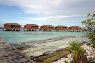 Tahta iskelesi ve küçük ahşap evleri olan bir sahil. Evlerin hepsi kırmızıya boyandı ve iskele boyunca dizildi. Su sakin ve gökyüzü berrak.