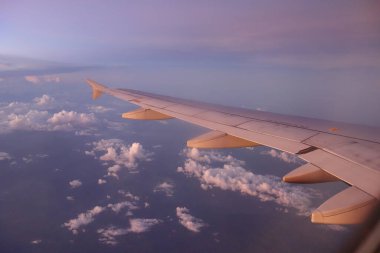Bir uçağın kanadı bulutlarla gökyüzünde görülür. Gökyüzü mavi ve pembenin karışımıdır.
