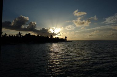 Güneş okyanusun üzerinde batıyor, suyun üzerine sıcak bir parıltı saçıyor. Gökyüzü bulutlarla dolu. Huzurlu ve huzurlu bir atmosfer yaratıyor.