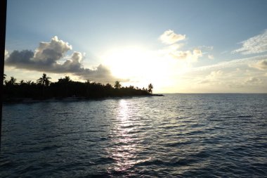Güneş okyanusun üzerinde batıyor, suyun üzerine sıcak bir parıltı saçıyor. Gökyüzü bulutlarla dolu, sakin ve huzurlu bir atmosfer yaratıyor. Sahne, deniz kenarında dinlenmek için mükemmel.