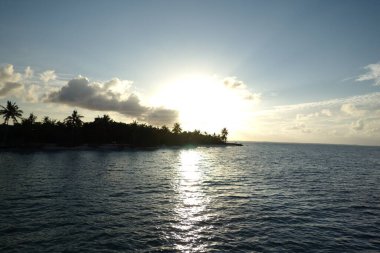 Güneş okyanusun üzerinde batıyor, suyun üzerine sıcak bir parıltı saçıyor. Gökyüzü mavi ve beyaz bulutların karışımıdır. Huzurlu ve huzurlu bir atmosfer yaratır.