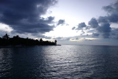 Gökyüzü bulutlu ve su sakin. Sahne huzurlu ve huzurlu. Bulutlar gökyüzünde alçaktır ve su koyu mavi renktedir. Arka plandaki ağaçlar uzun ve gür.