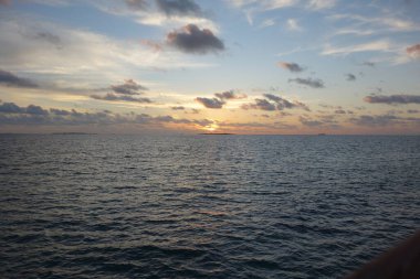 Gökyüzü, birkaç bulutun etrafa saçıldığı güzel bir mavi tondur. Güneş batıyor, okyanusun üzerine sıcak bir parıltı saçıyor. Su sakin ve durgun. Huzurlu bir atmosfer yaratıyor.