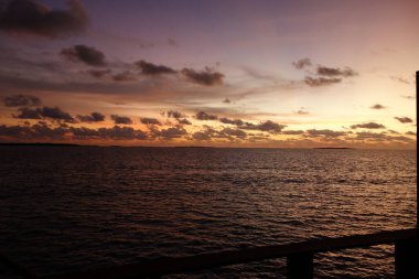 Güneş batarken gökyüzü güzel turuncu bir renktir. Su sakin ve bulutlar gökyüzüne dağılmış.