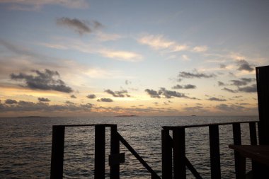 Güneş okyanusun üzerinde batarken gökyüzü turuncu ve pembe renklerin güzel bir karışımıdır. Su sakin ve ufukta kayıklar var. Sahne sakin ve huzurlu, okyanusla birlikte.