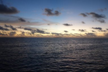 Gökyüzü birkaç bulutla güzel mavi bir renktir. Okyanus sakin ve huzurlu. Güneş batıyor, sıcak ve huzurlu bir atmosfer yaratıyor.