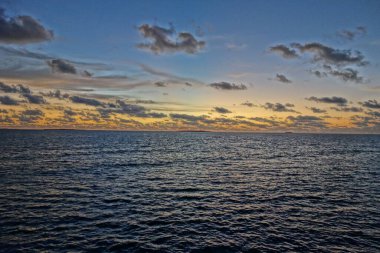 Gökyüzü birkaç bulutla güzel mavi bir renktir. Okyanus sakin ve huzurlu. Güneş batıyor, sıcak ve huzurlu bir atmosfer yaratıyor.