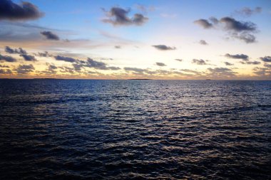Gökyüzü birkaç bulutla güzel mavi bir renktir. Okyanus sakin ve huzurlu. Güneş batıyor, sıcak ve huzurlu bir atmosfer yaratıyor.
