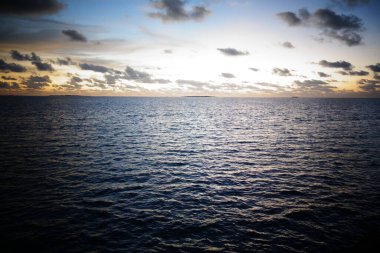 Okyanus sakin ve gökyüzü mavinin güzel bir tonu. Güneş batıyor, suyun üzerine sıcak bir parıltı saçıyor.