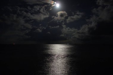 Ay suyun üzerinde parlıyor, huzurlu ve huzurlu bir atmosfer yaratıyor. Karanlık gökyüzü ve sakin su güzel ve rahatlatıcı bir manzara yaratır.