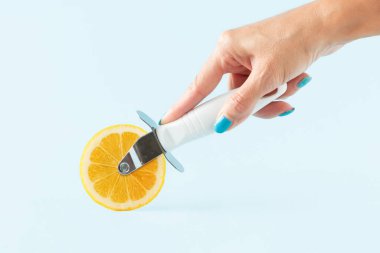 Kadın eli, izole edilmiş pastel mavi arka planda limon dilimli pizza kesicisini tutuyor. Sağlıklı yaşam tarzı ve C vitamini takviyesi için asgari estetik soyut bağışıklık sistemi konsepti. Sağlık ve Hastalık Önleme.
