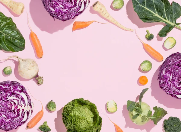 Winter vegetable food pattern. Collard greens, Swiss chard, carrots, parsnips, white radish, broccoli, Brussels sprouts, kohlrabi, red cabbage and kale on pink background. Healthy eating. Flat lay.