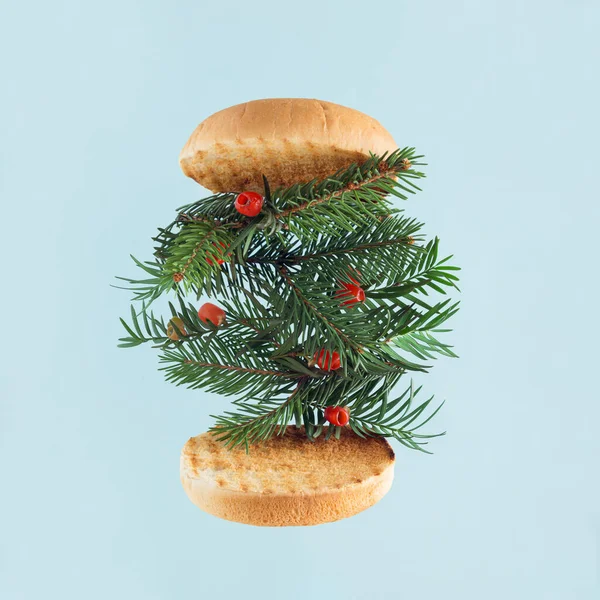 stock image Twigs with red berries evergreen common yew tree (Taxus Baccata) in halved toasted bun floating on pastel blue background. Natural Christmas decoration. Minimal creative abstract concept of Xmas card.