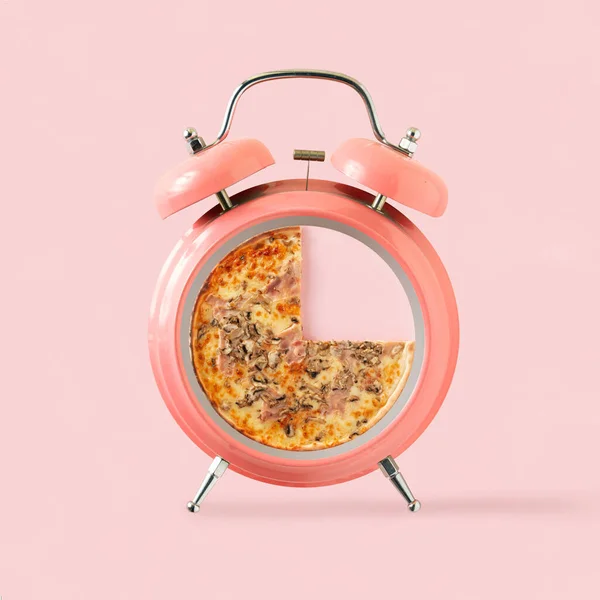 Slice of pizza in a coral pink alarm clock on isolated pastel background. Time for eating. Minimal creative abstract wallpaper.  Kitchen, pizzeria or restaurant card. Fast food catering concept.