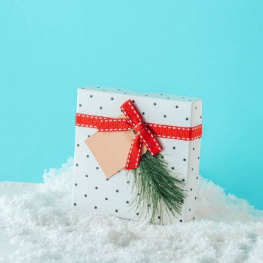 2023. Kırmızı kurdeleli dekoratif beyaz hediye kutusu ve karlı Noel ağacı dalı izole edilmiş pastel turkuaz mavi arka planda. Minimal yeni yıl kış sahnesi. Xmas kartı. Tatil kutlaması konsepti.