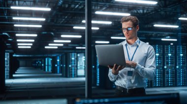 Teknoloji Araştırma Tesisi: Baş Mühendis Laboratuvarın Ortasında Duruyor ve Dizüstü Bilgisayar Kullanıyor. Akşamları E- İş Dijital Girişimcisi Bulut Web Servislerini İnceleyecek